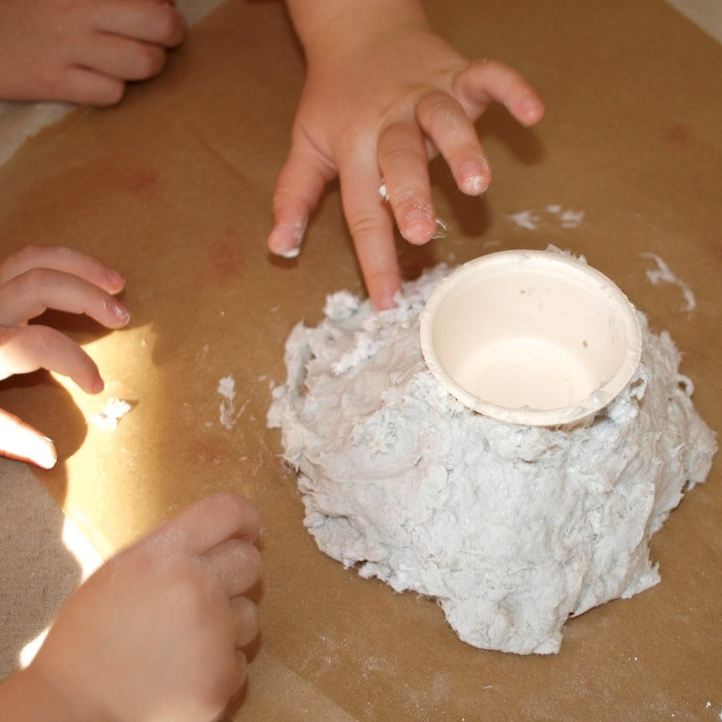 Children crafting a papier-mâché volcano model with a DIY kit on a brown table surface